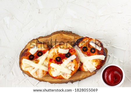 Mini pizza as mummy for kids with cheese, olives and ketchup. Funny crazy Halloween food for children on white background with copyspace