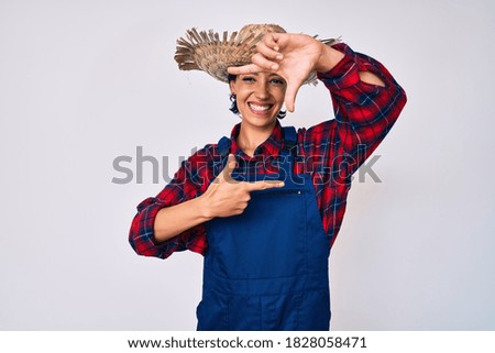 Beautiful brunettte woman wearing farmer clothes smiling making frame with hands and fingers with happy face. creativity and photography concept. 