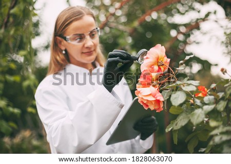 A botanist woman holding a tablet and a magnifying glass examines a plant sample during a quality check. Royalty-Free Stock Photo #1828063070