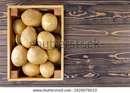 Wooden crate full of fresh raw potatoes on the wooden background with copy space. Top view.
