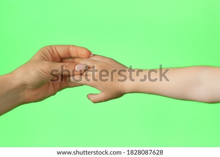 a woman's hand holds a child's palm on a green background, chromakey