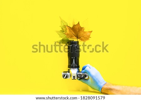 Up view of a Hand with blue gloves holding Vintage grey camera in yellow background. Autumn shooting