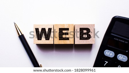 WEB is written on wooden cubes between a pen and a calculator on a light background. Internet concept