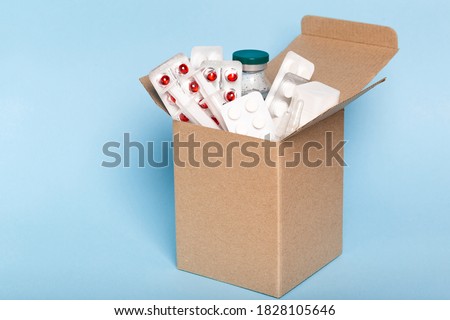 Delivery of medicines home from the pharmacy. Cardboard box with medicines, pills, bottles, injections isolated on blue background. Royalty-Free Stock Photo #1828105646