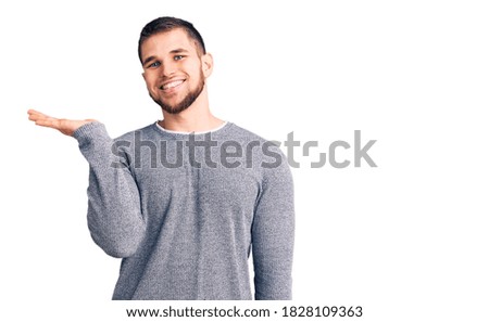 Young handsome man wearing casual sweater smiling cheerful presenting and pointing with palm of hand looking at the camera. 