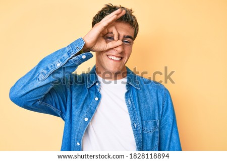 Young handsome man wearing casual clothes doing ok gesture with hand smiling, eye looking through fingers with happy face. 