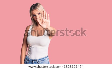 Young beautiful blonde woman wearing casual sleeveless t-shirt doing stop sing with palm of the hand. warning expression with negative and serious gesture on the face. 