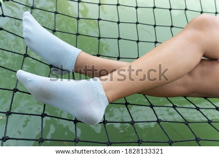 Legs of a woman with white socks lie on a net in a clear green body of water.
