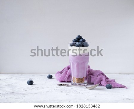 Cheesecake glass. Blueberry cheesecake in a glass with ripe blueberries, pink textiles and a spoon on a light background with space for text.