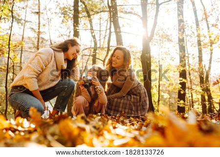 A young couple of lesbian ladies with her daughter  walking and and taking pictures in the autumn forest. Family spending time together. Autumn women.