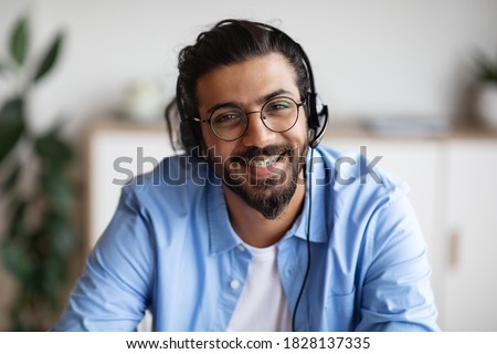 Call Center Operator. Closeup portrait of positive indian man customer service representative in headset, handsome western guy hotline manager looking at camera and smiling, selective focus Royalty-Free Stock Photo #1828137335