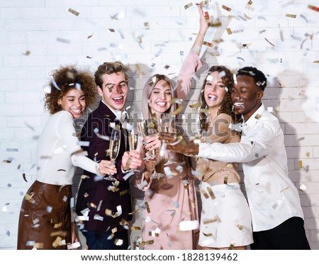 Party Concept. Diverse Guys And Girls Clinking Glasses Under Falling Confetti Celebrating Holiday Indoor.
