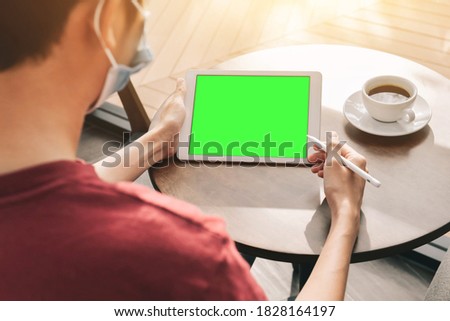 a man working on green screen tablet on table near coffee cup  he use tablet pen in coffee cafe , summer and use mask covid-19