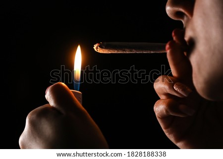 Woman hand holding cigarette in a smoke against black background. Smoking cannabis joint. Medical use. Royalty-Free Stock Photo #1828188338