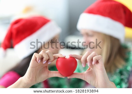 Women in santa claus hats hold red heart toy close-up. Wishes for christmas and new years concept.