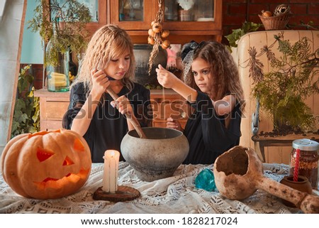 Two cute girls aged 9 years in witch costumes in an old house on Halloween brew a magic potion and conjure. The concept of witchcraft, evil spirits, and a fabulous fall holiday Halloween