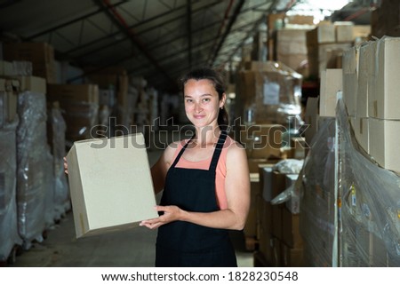 Happy female seller holding box in warehouse. High quality photo