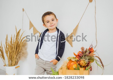A little boy holds his hands in his pockets against the background of autumn decor. Children's photo zone in autumn style with pumpkins.
