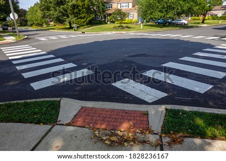 White rectangular intermittent crosswalk markers painted on the asphalt road in a residential neighborhood
