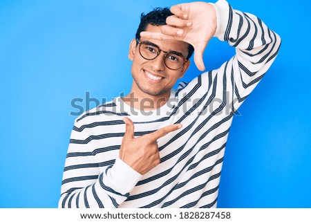 Young handsome hispanic man wearing casual sweater and glasses smiling making frame with hands and fingers with happy face. creativity and photography concept. 