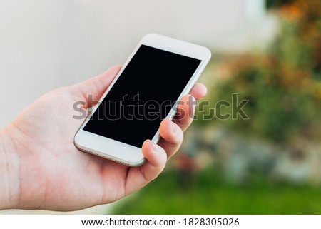Cropped shot of male hands holding smartphone with blank screen copy space for your text message or informational content, reading text message on cell phone against green nature background