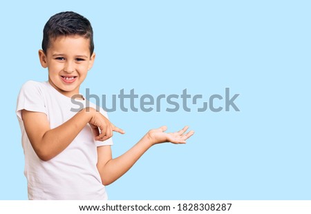 Little cute boy kid wearing casual white tshirt amazed and smiling to the camera while presenting with hand and pointing with finger. 