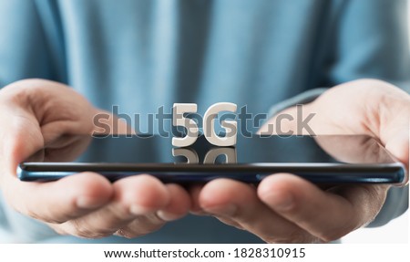 Mobile phone, smartphone with 5 G wireless high speed internet in hands of man. Creative big white letters 5G on touch screen,reflection. Connection for home, work, business.Modern technology concept. Royalty-Free Stock Photo #1828310915
