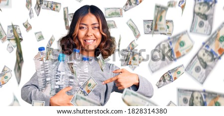 Young beautiful mixed race woman holding recycling plastic bottles smiling happy pointing with hand and finger