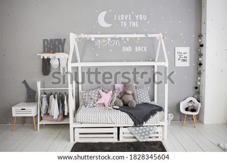 Child's bedroom, modern design with neutral grey tones. Wooden bed with boxes for linen, pillows, rug, clothes hangers, chair, toys, writing on wall