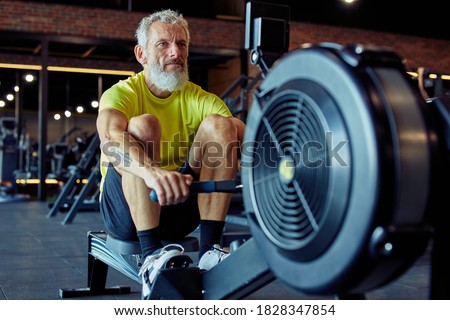 Sport and fitness after 50. Strong mature athletic man in sportswear exercising on rowing machine at gym Royalty-Free Stock Photo #1828347854