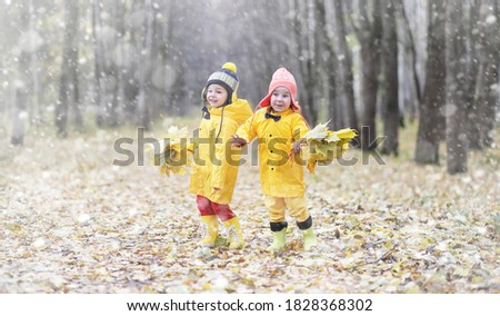 Toddlers walk in the autumn park. First frost and the first snow in the autumn forest. Children play in the park with snow and leaves.
