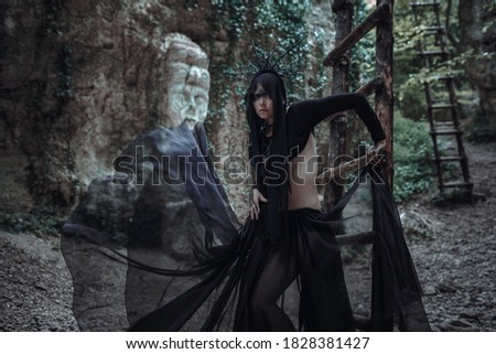 Mysterious sorceress woman witch beautiful black dress walk in dark forest. lady in Gothic look. Outfit for halloween.