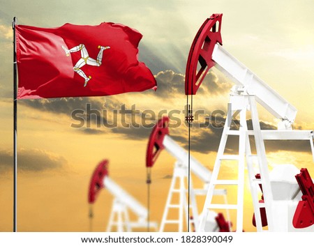 Oil rigs against the backdrop of the colorful sky and a flagpole with the flag of Isle Of Man. The concept of oil production, minerals, development of new deposits.