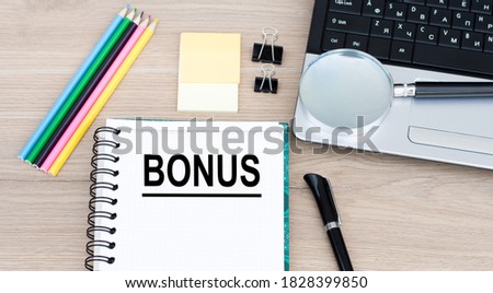 Office table with laptop, pen and blank notepad with BONUS text