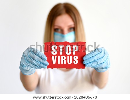 Young woman in mask and medical gloves holds red paper with the word "Stop Virus". Coronavirus danger concept. Global call to stay home