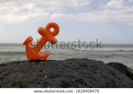 Orange anchor toy placed on a black stone with the australian ocean in the background, taken at Coolangatta beach in Queensland, Australia