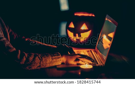 Halloween evening at the computer. Woman talking on the feast of Halloween on the internet. Coronavirus pandemic time concept. Shallow depth of field and noise. Royalty-Free Stock Photo #1828415744