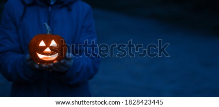 Jack o lantern glowing with moonlight in an eerie night forest.Halloween dark midnight background with burning orange pumpkin that a women holds in her hands.Happy Halloween card.Copyspace for text   