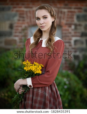 Portrait of a cute girl with a bouquet of yellow flowers on a brick wall background