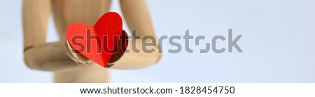 Red paper heart in hands of a wooden mannequin on a gray background. Trendy minimal concept of Valentine's day, love, real feeling. Banner.