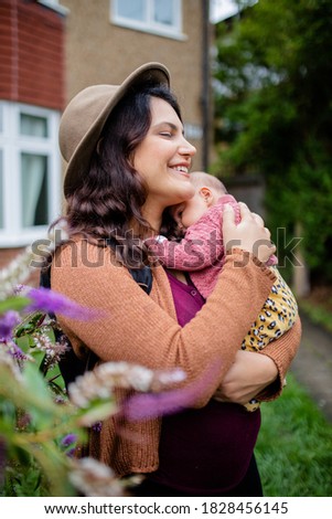 Smiling Mother Holding Her Baby Girl on Her Arms with a Building as Background