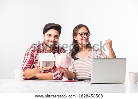 Focused Indian young couple accounting, calculating bills, discussing planning budget together using online banking services and calculator, checking finances