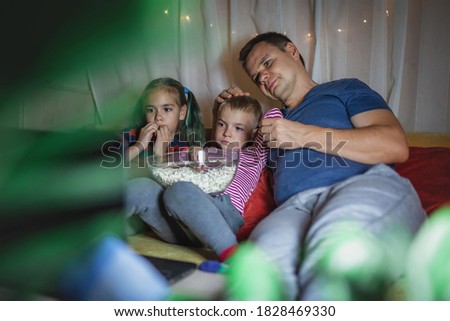 Family movie night. Father with kids sitting on couch and watching movie with popcorn by laptop at home, family entertainment, happy time together, childhood and entertainment, indoor lifestyle