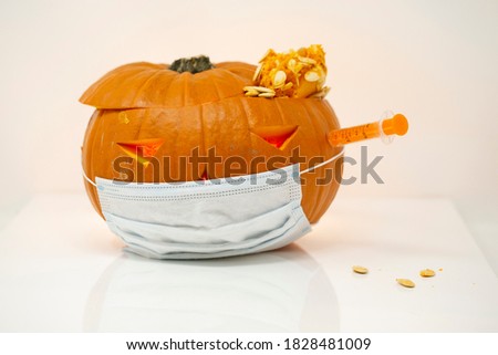 
Carved Halloween pumpkin with the mask on and a syringe stuck in it placed on the reflective table in the white background