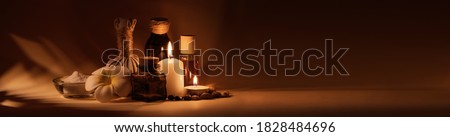 Beautiful spa composition with candles, frangipani flower, oil flasks, bowl with salt and herbal ball. Nice warm dark background. Tropical highlights from window. Copy space.