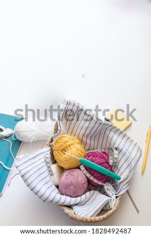 Overhead view of some colorful yarn balls inside a wicker chest . A green sewing needle and a sewing meter are at the top.