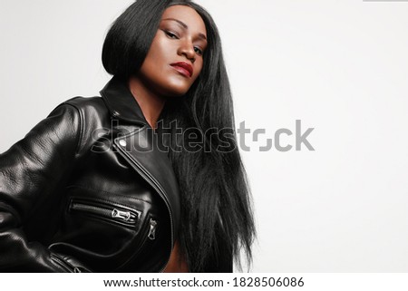 Close-up portrait of young attractive black woman wearing a leather jacket against white wall. Space for text.