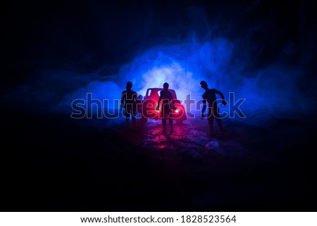 photo of a car stopped on the road lighting up a zombies. Silhouette terrible zombie night near the car. Miniature decoration. Selective focus