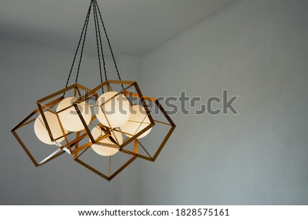 A round lamp with a rectangular iron frame suspended from the ceiling, illuminating in gold. Interior concept. Royalty-Free Stock Photo #1828575161