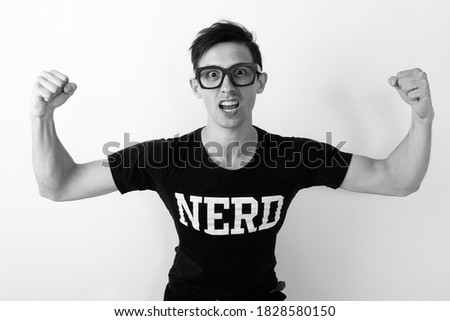 Studio shot of young nerd man flexing both arms while wearing eyeglasses against white background